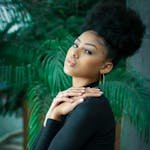 Stylish woman with natural curly hair in a lush indoor setting.